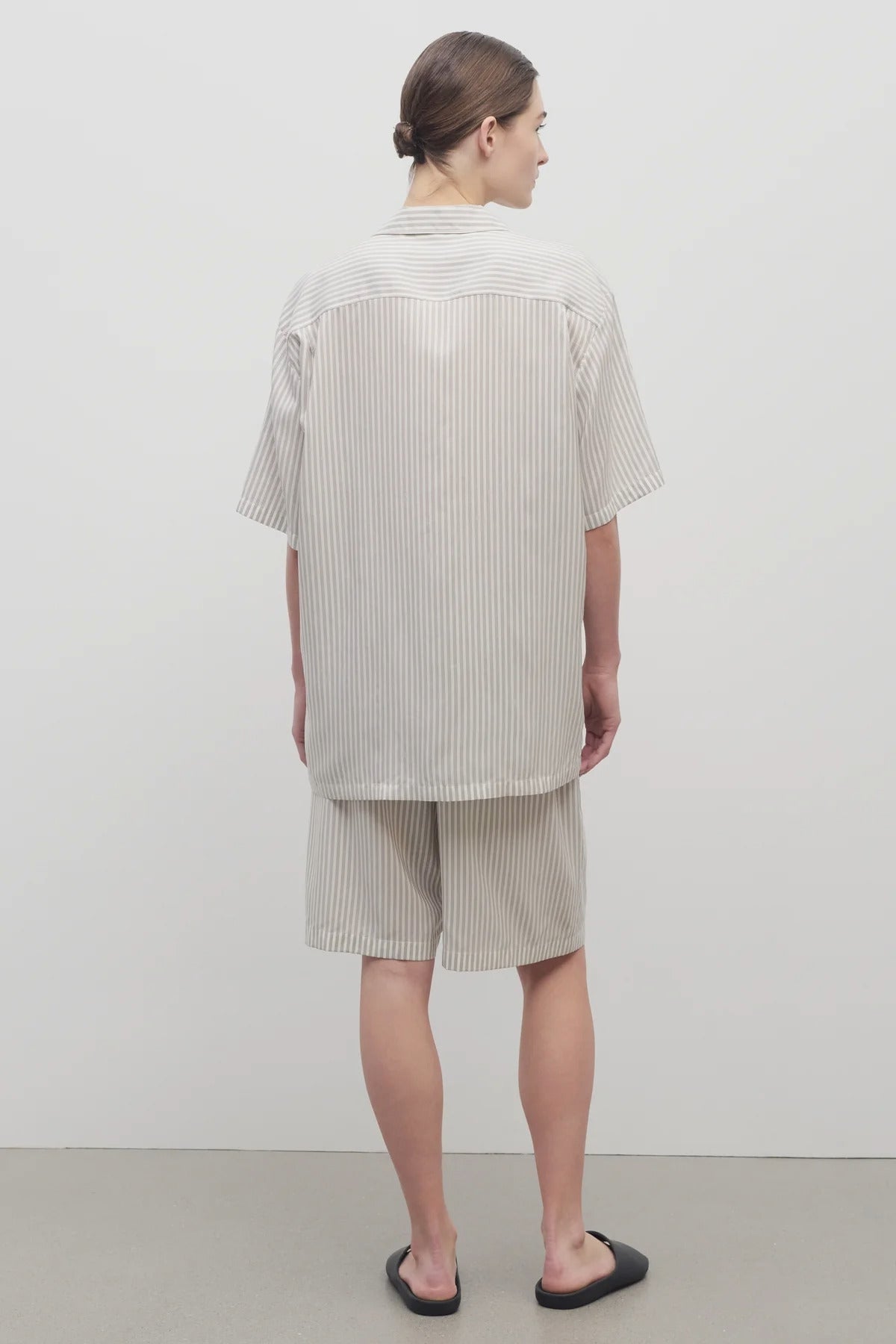 Back view of short with white background, on light brown haired model, worn with matching silk shirt and black sandals.