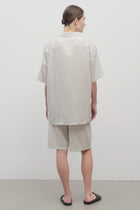 Back view of short with white background, on light brown haired model, worn with matching silk shirt and black sandals.