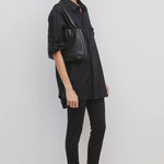 Side view of black woolworth on model wearing black tunic and black sandals, against a white background.