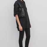 Side view of black woolworth on model wearing black tunic and black sandals, against a white background.