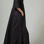 Side view of black rachel long dress on model wearing black flats, against a white background.