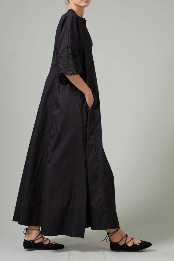 Side view of black rachel long dress on model wearing black flats, against a white background.