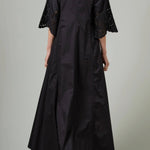 Back view of black rachel long dress on model wearing black flats, against a white background.