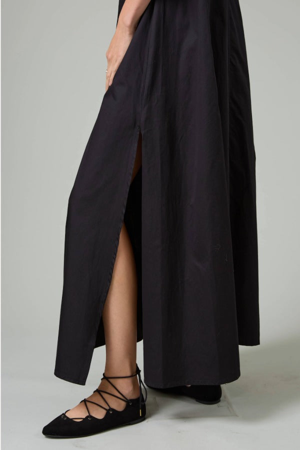 Alternate side closeup view of black rachel long dress on model wearing black flats, against a white background.