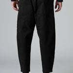 Back view of black japanese tobi trousers on model wearing a black top and boots, against a grey background.
