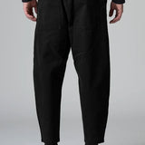 Back view of black japanese tobi trousers on model wearing a black top and boots, against a grey background.