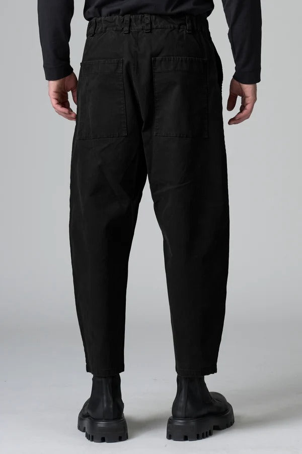 Back view of black japanese tobi trousers on model wearing a black top and boots, against a grey background.