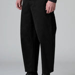 Side view of black japanese tobi trousers on model wearing black top and boots, against a grey background.