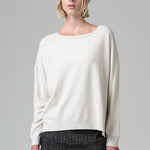 Front view of camel knitted cap on model wearing white top and stripe skirt, against a grey background.