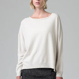 Front view of camel knitted cap on model wearing white top and stripe skirt, against a grey background.