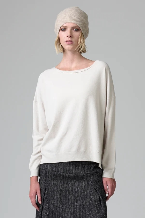 Front view of camel knitted cap on model wearing white top and stripe skirt, against a grey background.