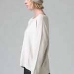 Side view of camel knitted cap on model wearing white top and stripe skirt, against a grey background.