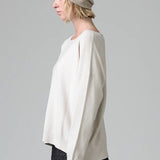 Side view of camel knitted cap on model wearing white top and stripe skirt, against a grey background.
