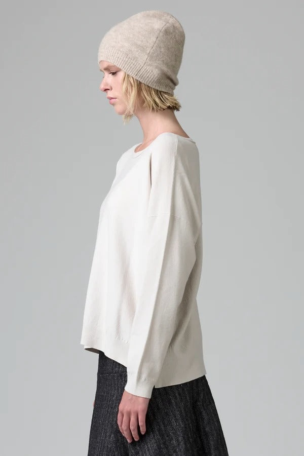 Side view of camel knitted cap on model wearing white top and stripe skirt, against a grey background.