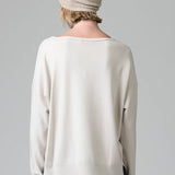 Back view of camel knitted cap on model wearing white top and stripe skirt, against a grey background.