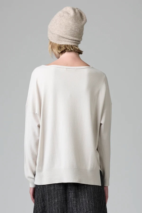 Back view of camel knitted cap on model wearing white top and stripe skirt, against a grey background.