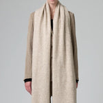 Front view of camel knitted scarf on model wearing matching camel suit, against a grey background.