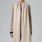 Front view of camel knitted scarf on model wearing matching camel suit, against a grey background.