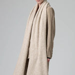 Side view of camel knitted scarf on model wearing matching camel suit, against a grey background.