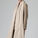 Side view of camel knitted scarf on model wearing matching camel suit, against a grey background.