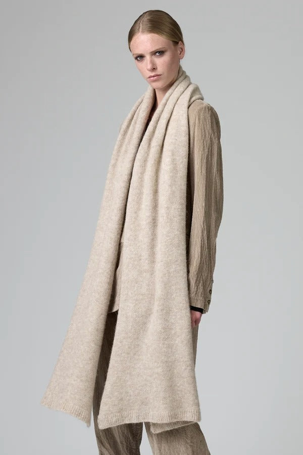 Side view of camel knitted scarf on model wearing matching camel suit, against a grey background.