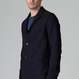 Side view of blue wool regular jacket on model wearing blue shirt and pants, against a grey background.