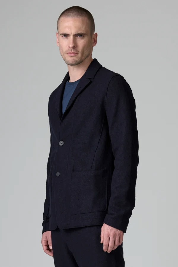 Side view of blue wool regular jacket on model wearing blue shirt and pants, against a grey background.