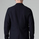 Back view of blue wool regular jacket on model wearing blue pants, against a grey background.