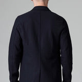 Back view of blue wool regular jacket on model wearing blue pants, against a grey background.