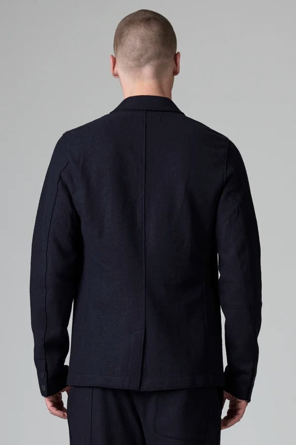 Back view of blue wool regular jacket on model wearing blue pants, against a grey background.