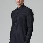 Side slanted view of blue loose fit striped shirt on model wearing black pants, against a grey background.
