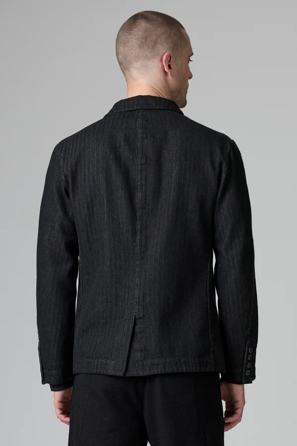 Back view of black regular 2 button jacket on model wearing black pants, against a grey background.