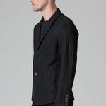 Side view of black regular 2 button jacket on model wearing black top and pants, against a grey background.