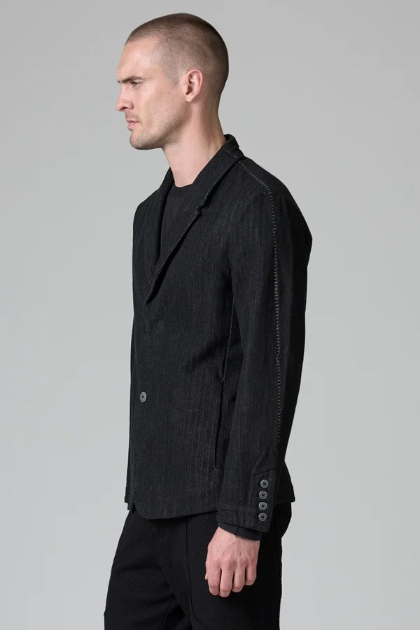 Side view of black regular 2 button jacket on model wearing black top and pants, against a grey background.