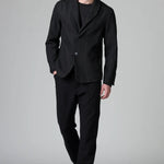 Front view of black regular 2 button jacket on model wearing black top, pants and boots, against a grey background.
