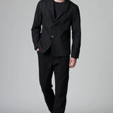 Front view of black regular 2 button jacket on model wearing black top, pants and boots, against a grey background.