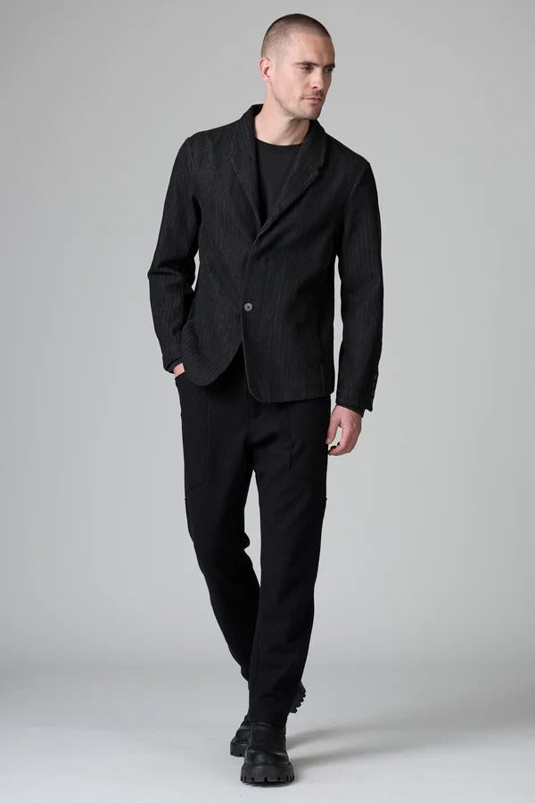 Front view of black regular 2 button jacket on model wearing black top, pants and boots, against a grey background.