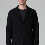 Front view of black/brown regular fit jacket on model wearing black pants, against a grey background.