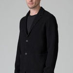 Side view of black/brown regular fit jacket on model wearing black pants, against a grey background.