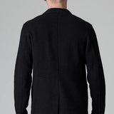 Back view of black/brown regular fit jacket on model wearing black pants, against a grey background.