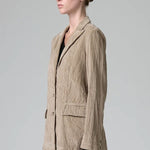 Side view of camel regular fit jacket on model wearing camel pants and black top, against a grey background.
