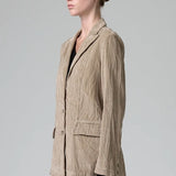 Side view of camel regular fit jacket on model wearing camel pants and black top, against a grey background.