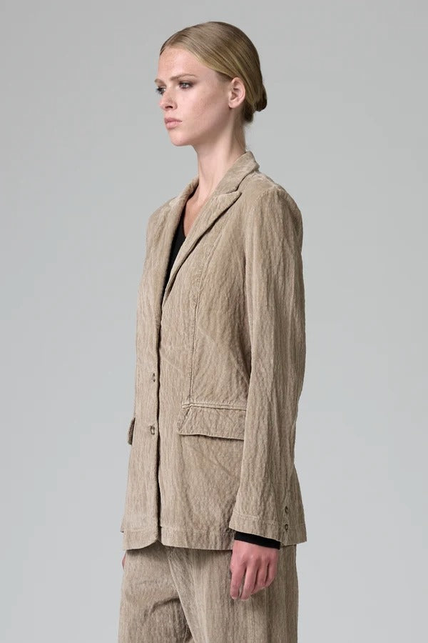 Side view of camel regular fit jacket on model wearing camel pants and black top, against a grey background.