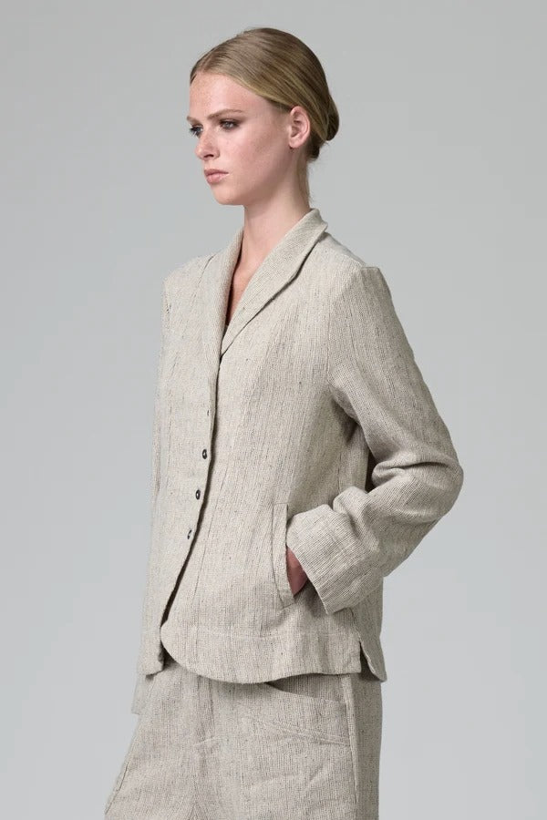 Side view of chalk herringbone jacket on model wearing chalk pants, against a grey background.