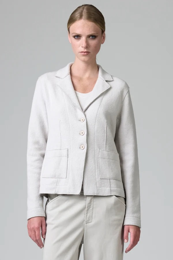 Front view of chalk/grey shaped knitted jacket on model wearing chalk pants, against a grey background.