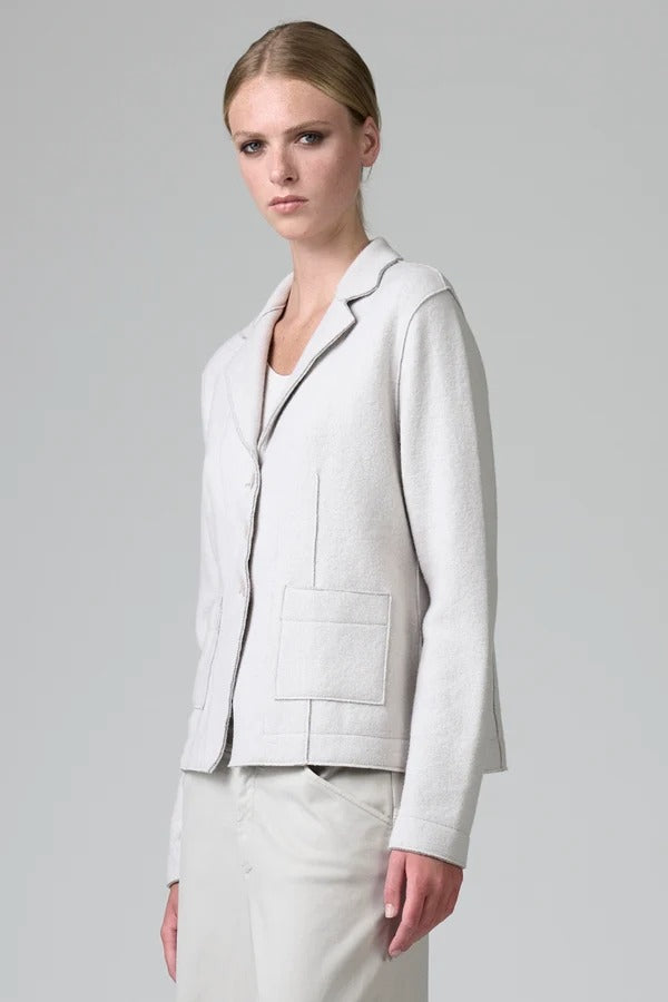 Side view of chalk/grey shaped knitted jacket on model wearing chalk pants, against a grey background.