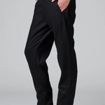 Side view of black slim fit trousers on model wearing black top and boots, against a grey background.