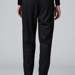 Back view of black slim fit trousers on model wearing black top and boots, against a grey background.