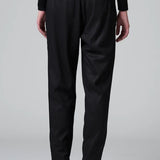 Back view of black slim fit trousers on model wearing black top and boots, against a grey background.