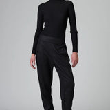 Front view of black slim fit trousers on model wearing black top and boots, against a grey background.